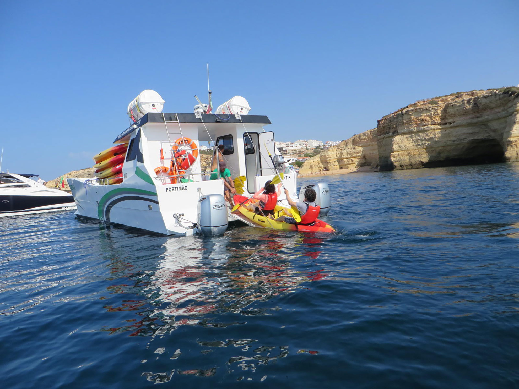 Kayaking tour near Benagil with catamaran support vessel, Algarve coastline in background