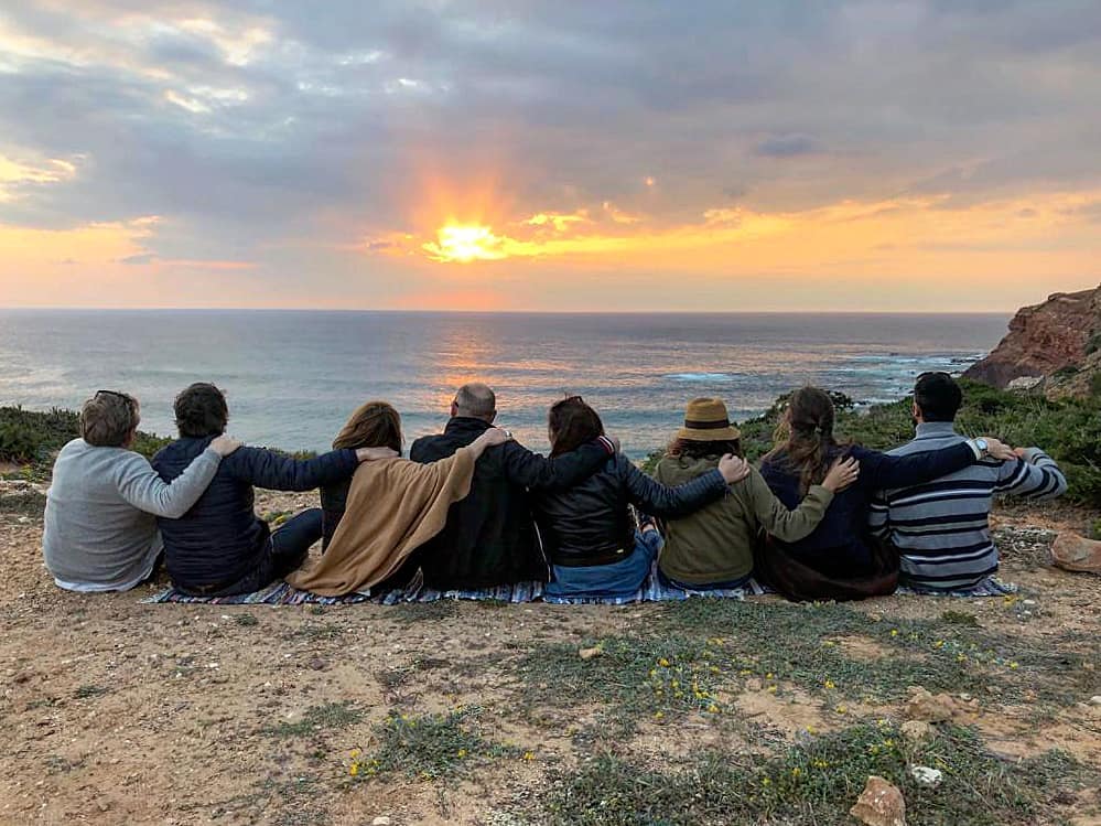 Group of friends watching the sunset from a boat in the Algarve, glasses of wine in hand