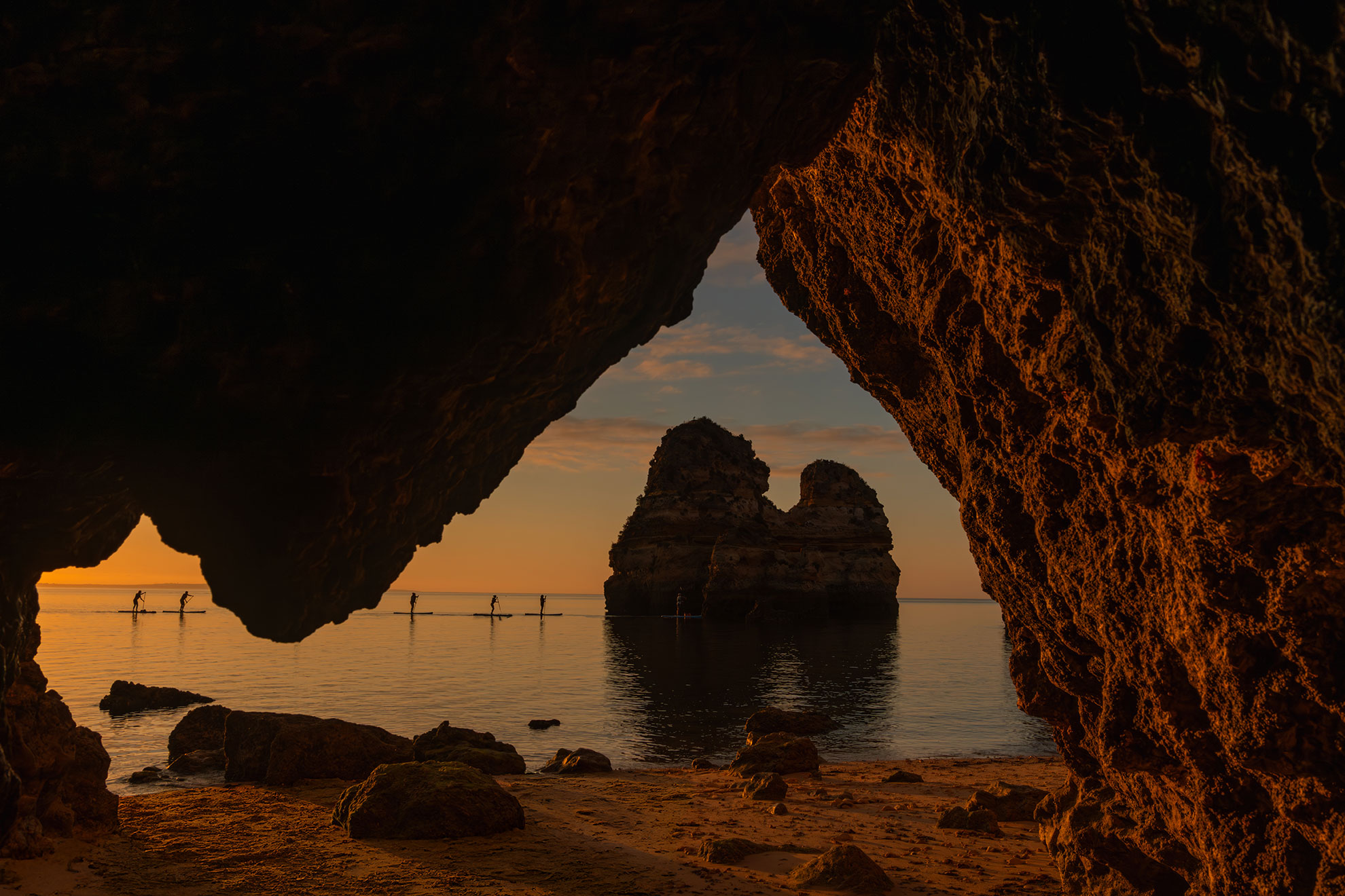 Kayaker inside a sea cave near Lagos, natural light filtering through the cave entrance onto turquoise water