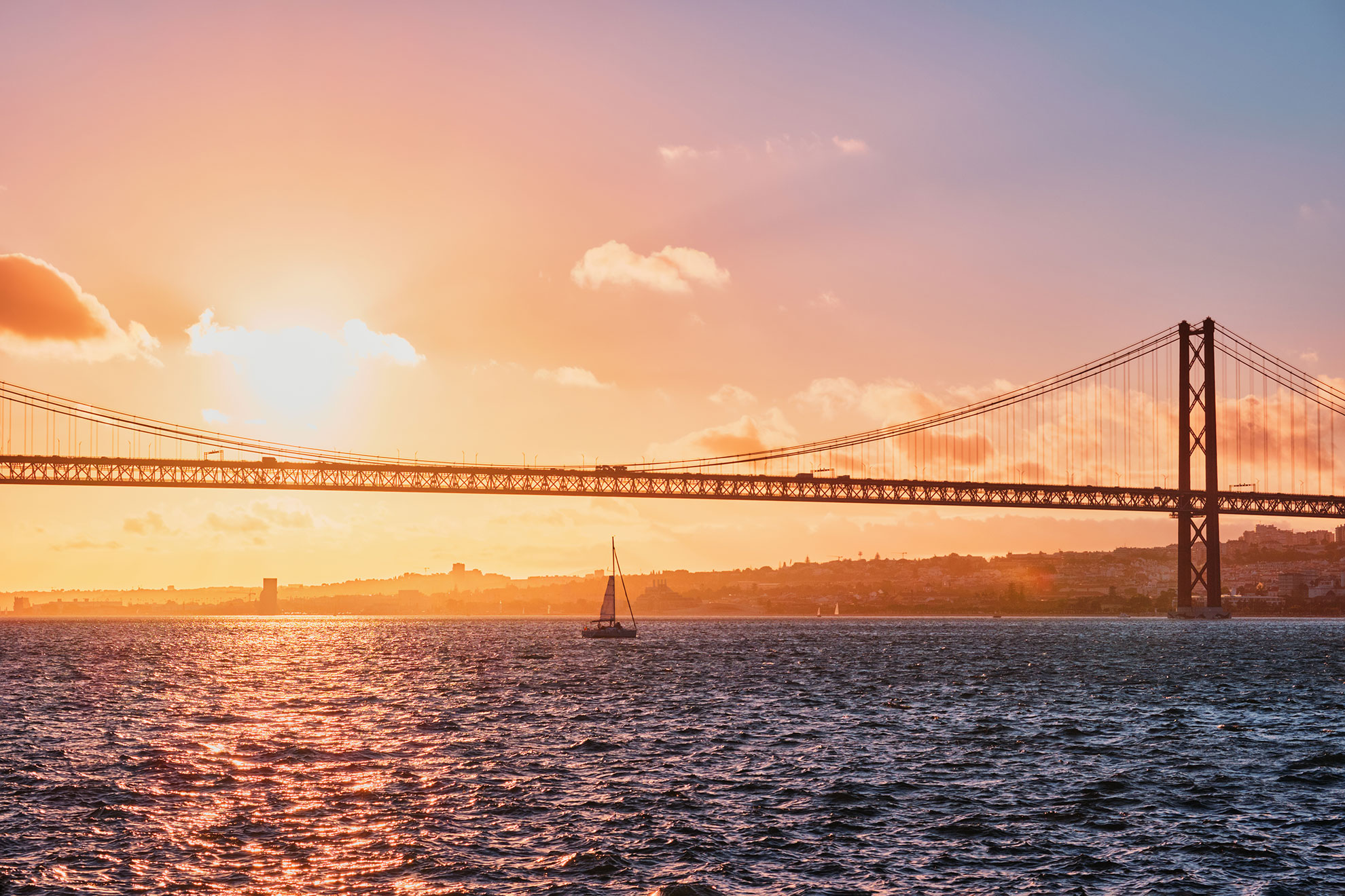 Sailing boat on the Tagus river at sunset with the Lisbon skyline and 25 de Abril bridge in the background