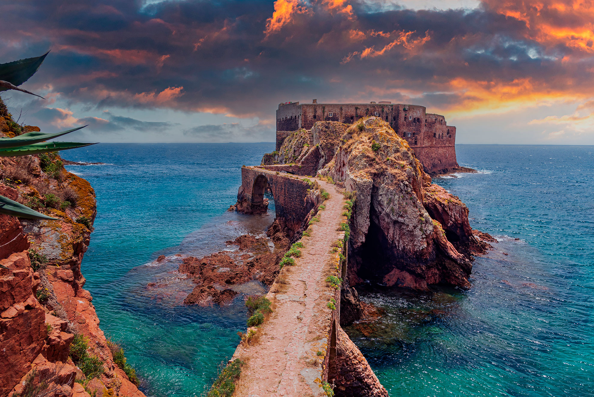 Forte de São João Baptista on its granite islet, connected by a stone arch bridge over clear turquoise water