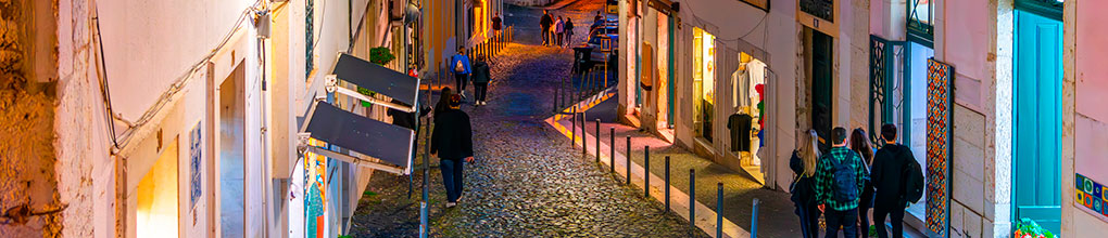 Narrow cobblestone street in Alfama at night with fado music audible from a nearby taberna