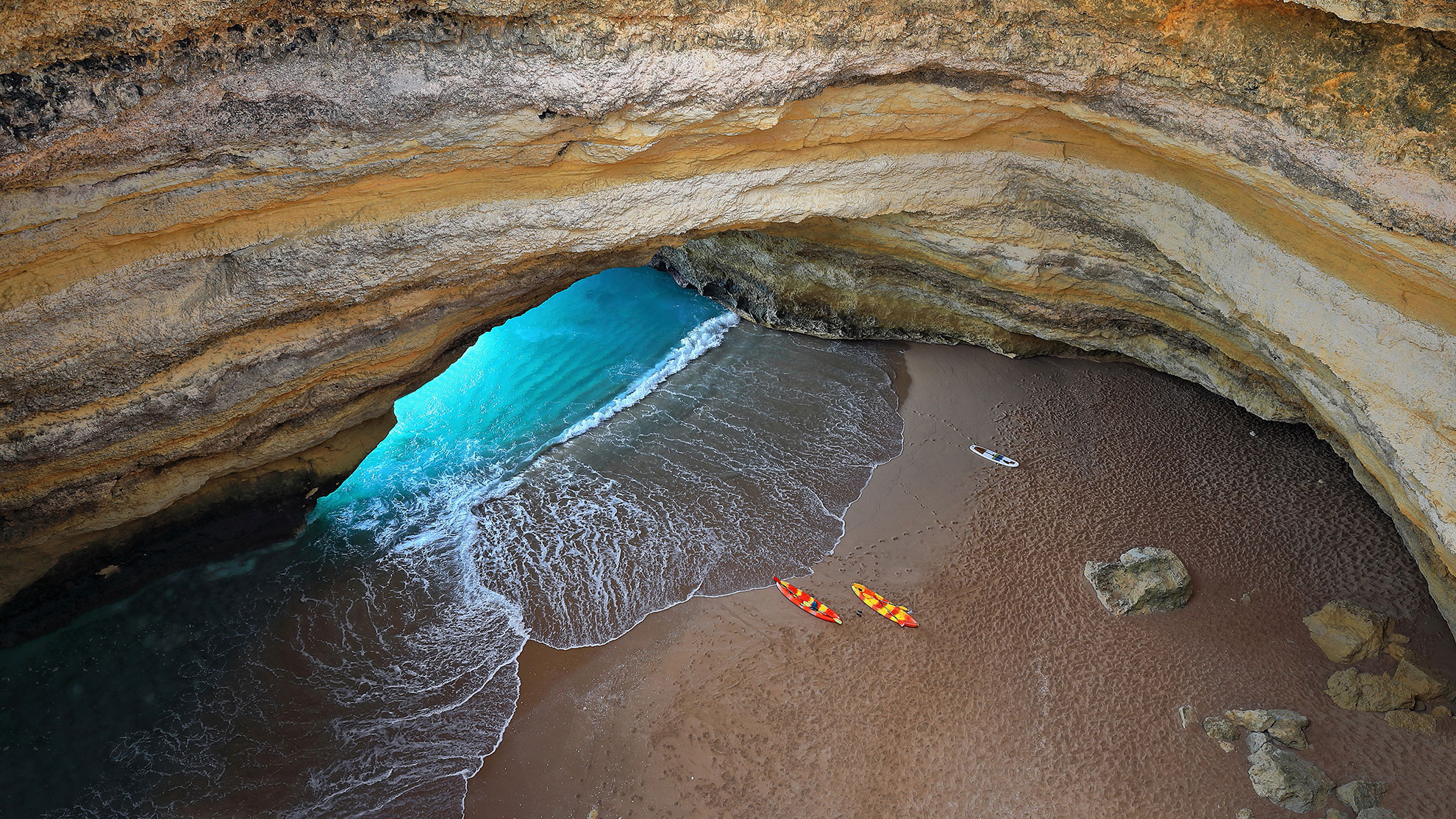 Two kayaks floating on emerald water inside a limestone sea cave near Benagil