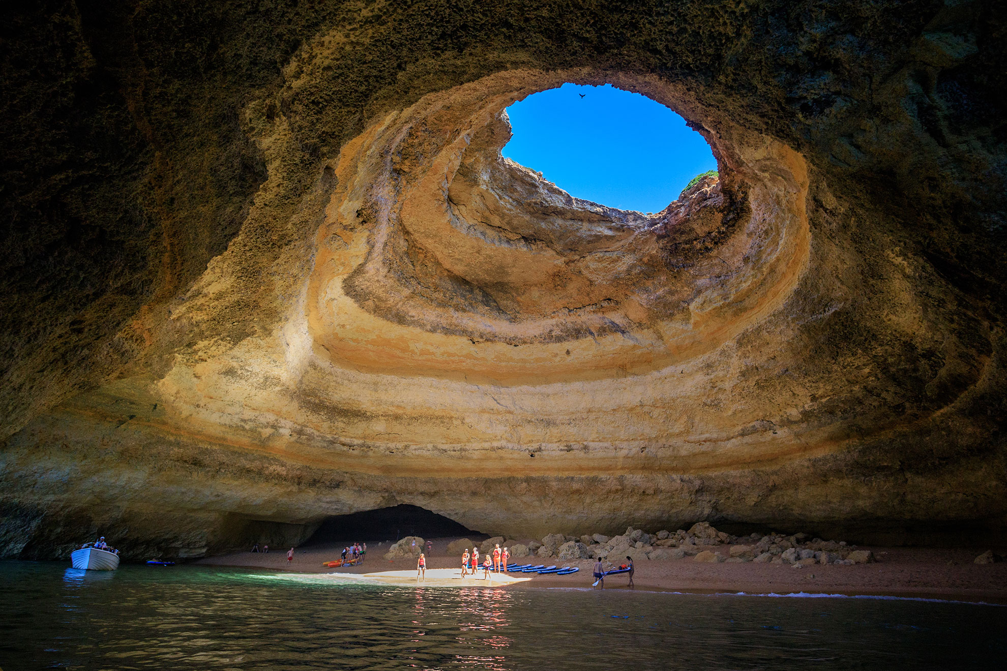 Inside Benagil Cave with sunlight streaming through the circular ceiling opening onto the secret sandy beach