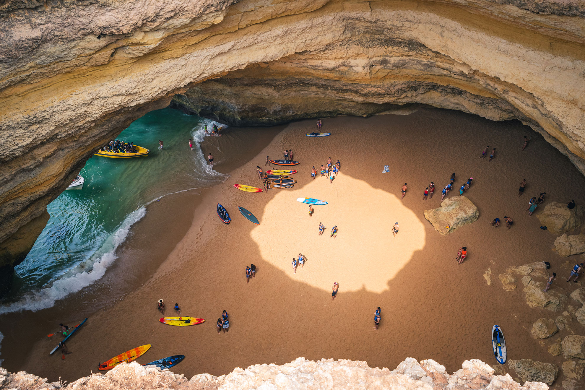 Shafts of sunlight entering through the ceiling aperture of Benagil Cave illuminating the turquoise water below