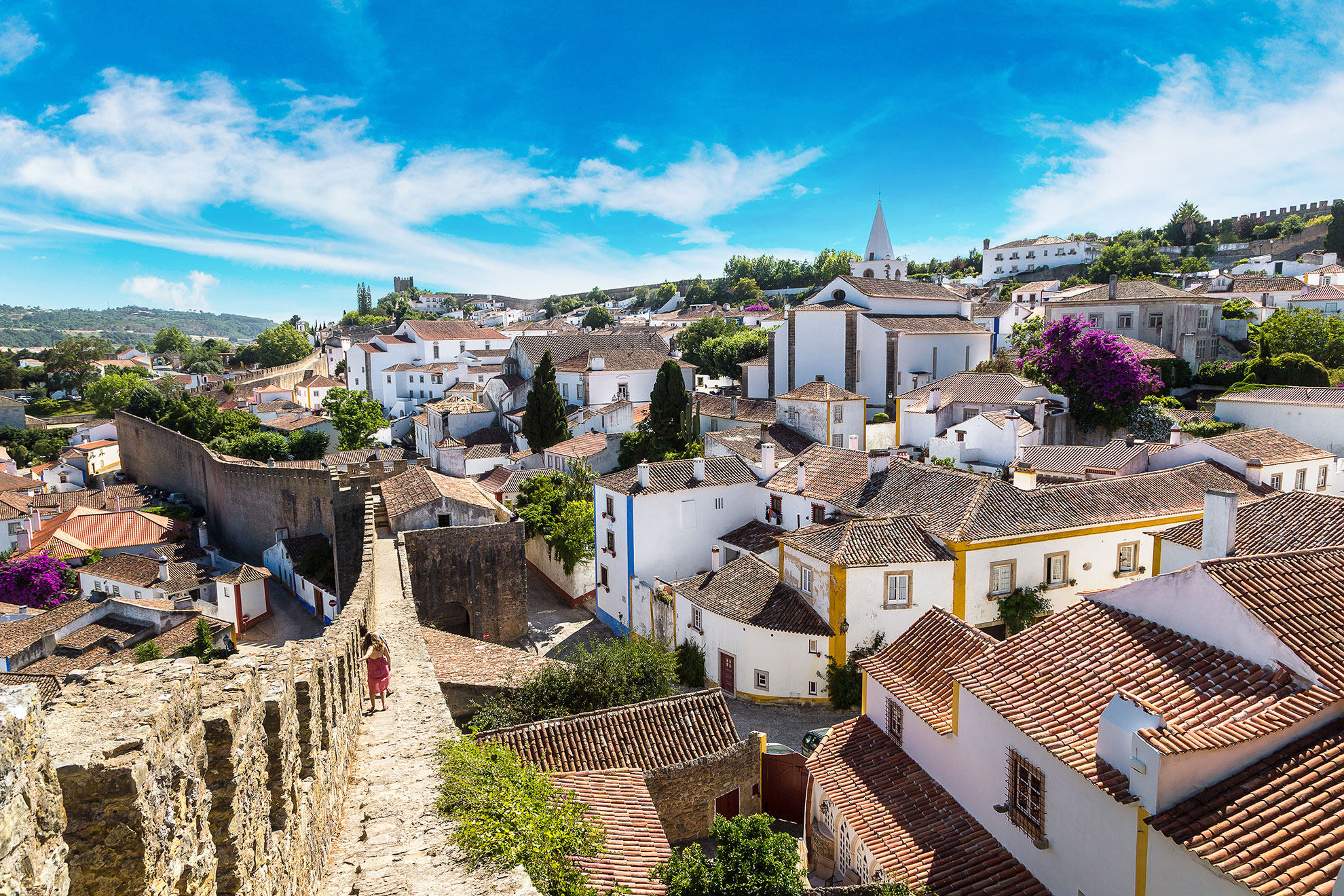 Visitors walking along the narrow top of Óbidos' ancient stone ramparts with countryside views beyond