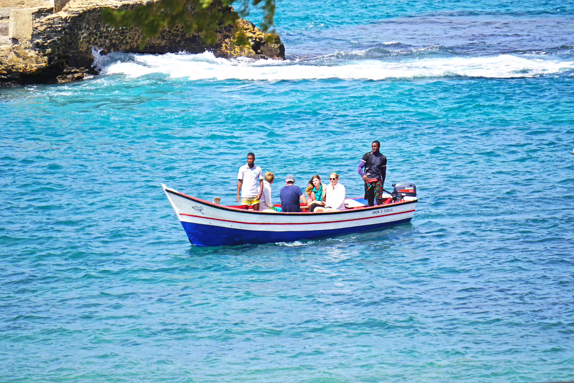 A small boat approaching a dramatic sea cave on the Cape Verde coastline, the turquoise Atlantic water glowing in the cave entrance, snorkellers below the surface