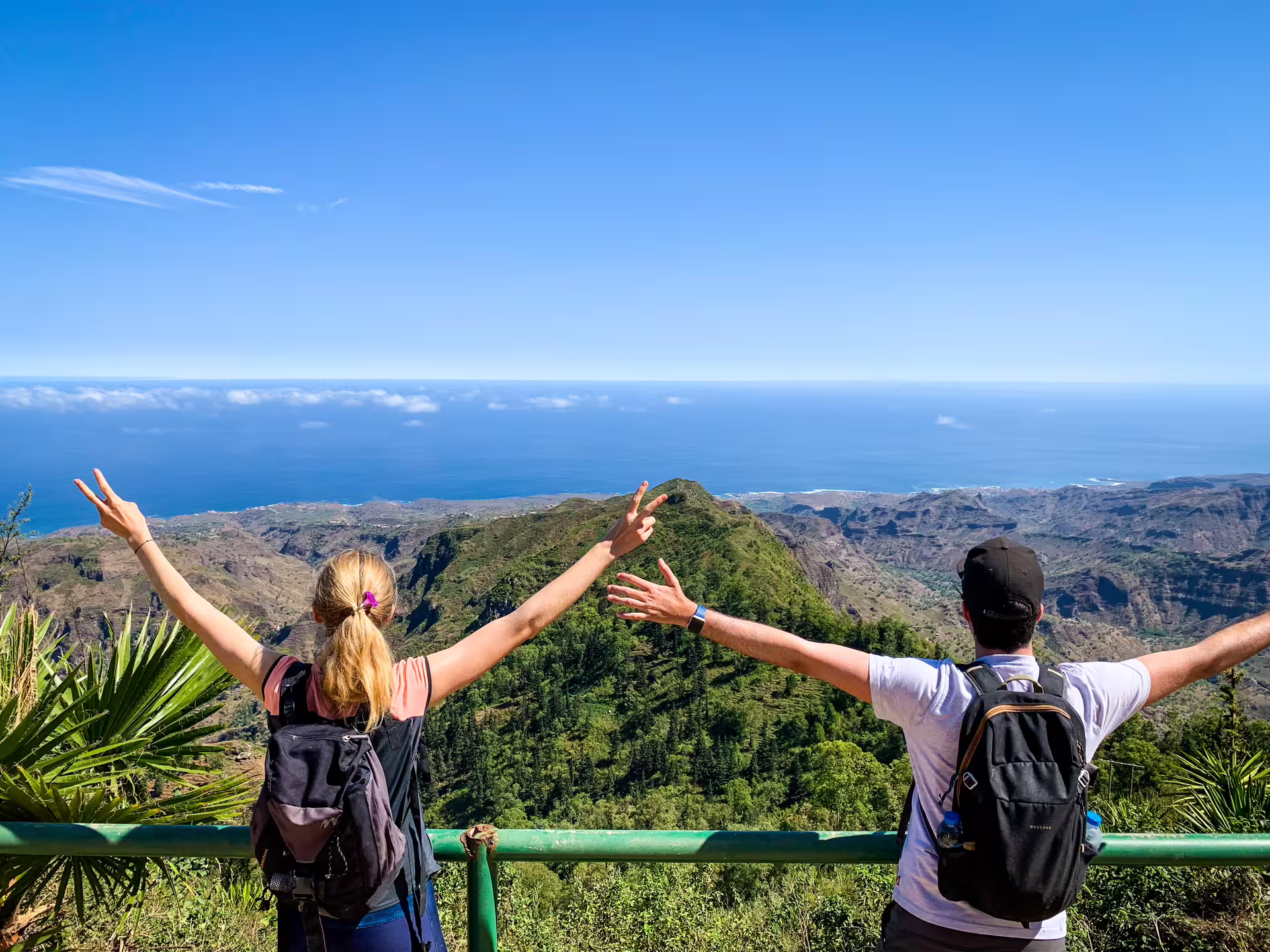 Hikers on a lush green trail descending through Serra Malagueta Natural Park on Santiago Island, with misty mountain ridges and the Principal Valley visible in the background