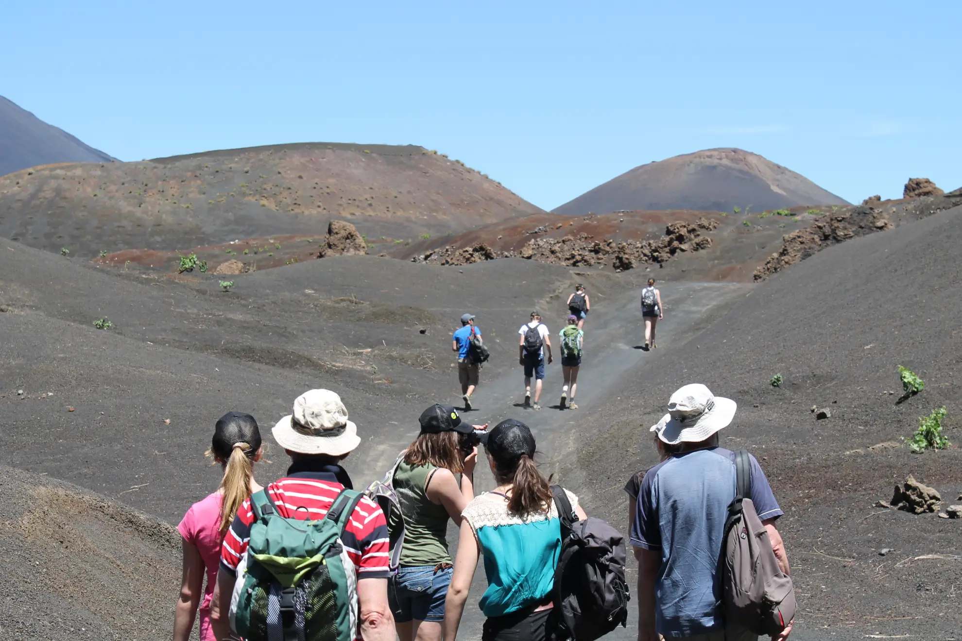 Hikers ascending the steep loose volcanic ash and lava rock of Pico do Fogo at high altitude on Fogo Island, Cape Verde, with the vast Atlantic Ocean visible far below and cloud formations at eye level
