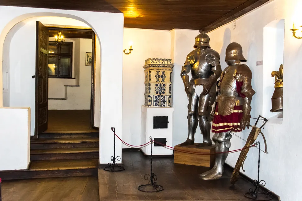 Una sala de paredes blancas en el Castillo de Bran con armaduras y una estufa de azulejos