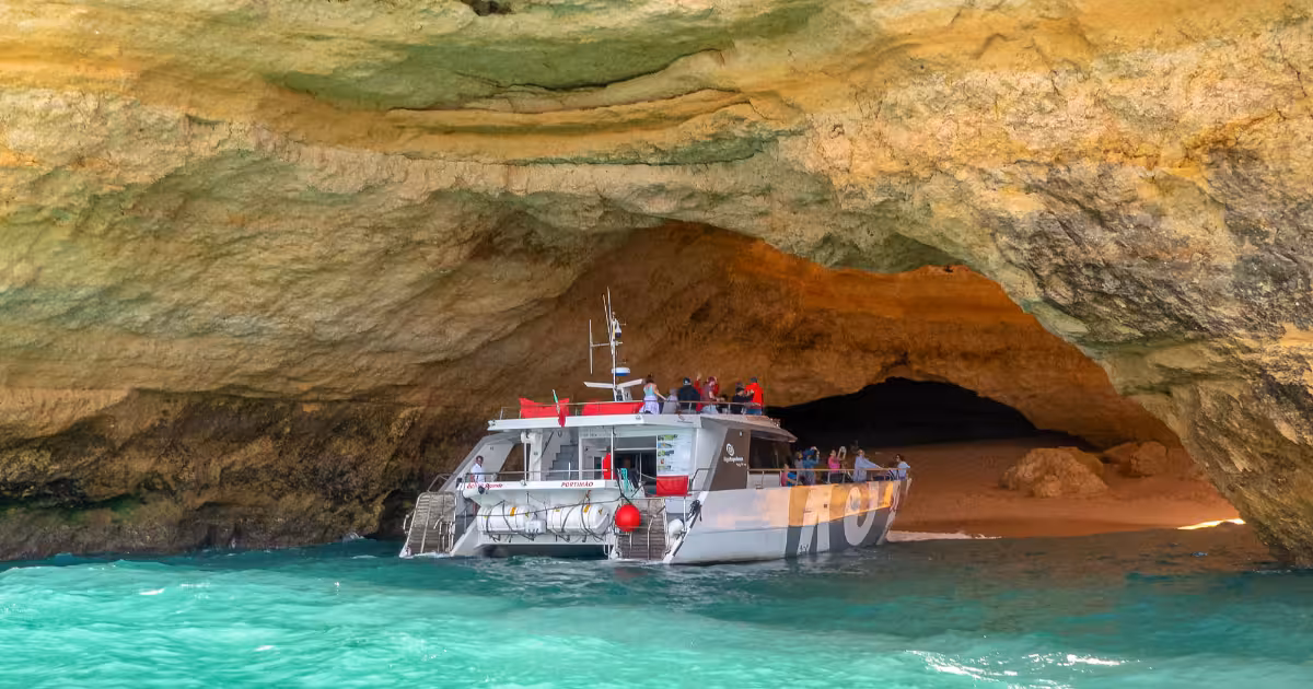 Luxury catamaran sailing along Algarve golden limestone cliffs near Albufeira.