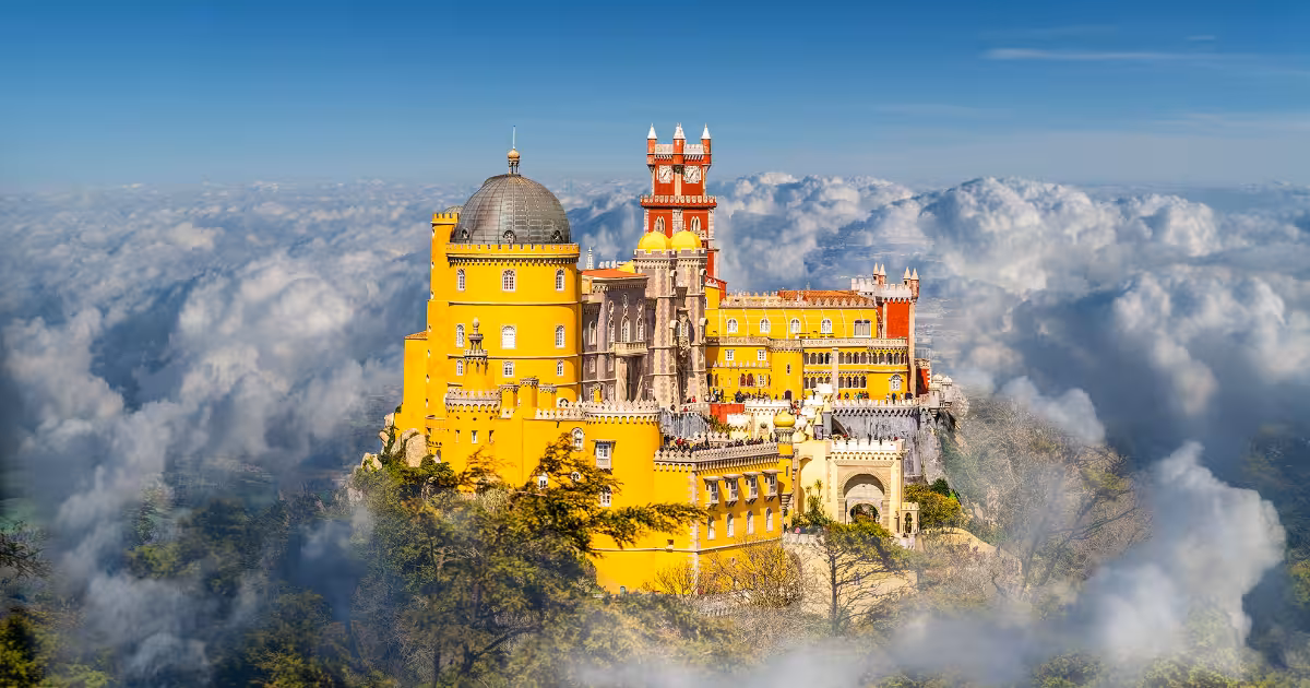 Pena Palace colorful towers emerging from morning mist above Sintra forest.