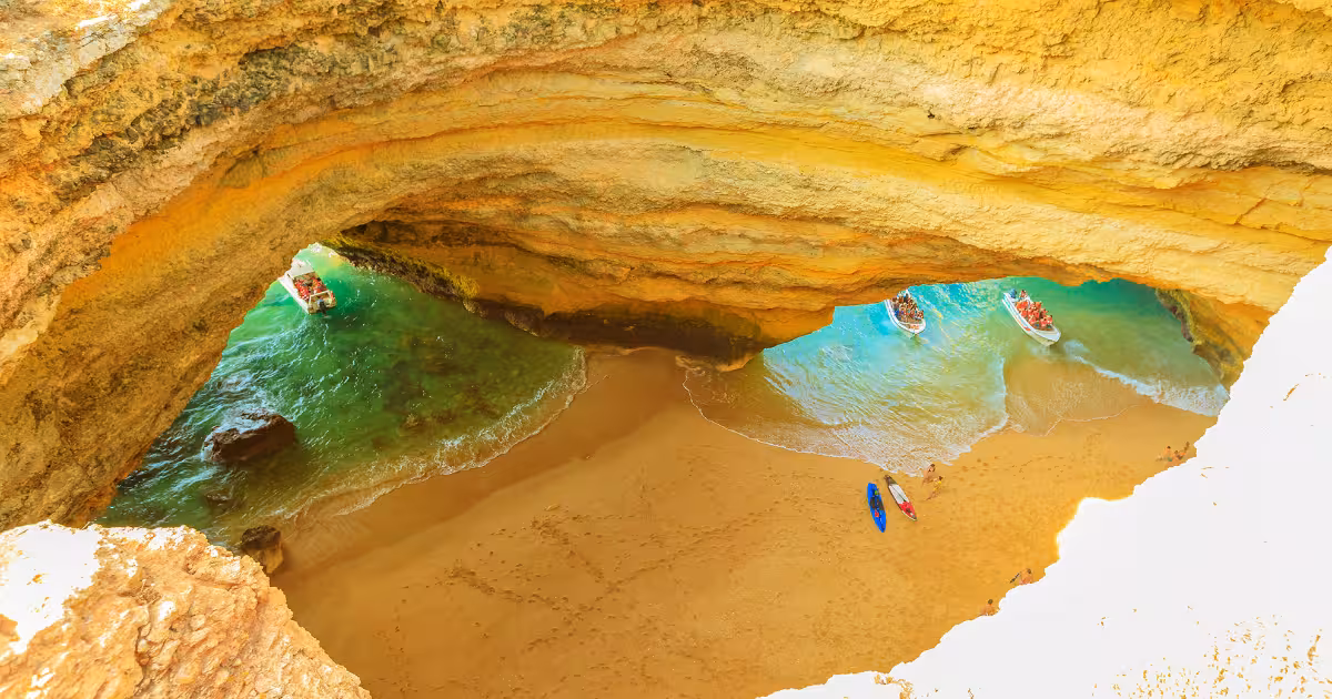 Sunlight streaming through Benagil Cave's skylight onto turquoise water and sand