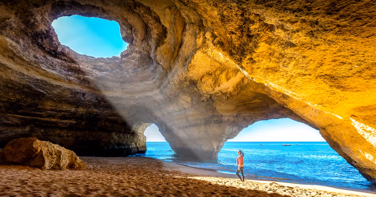 Kayaker paddling through sunlit Benagil Cave arch on calm turquoise water.
