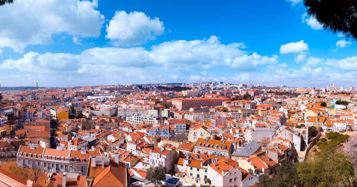 Lisbon rooftops and the Tagus River seen from a hilltop miradouro at sunset.