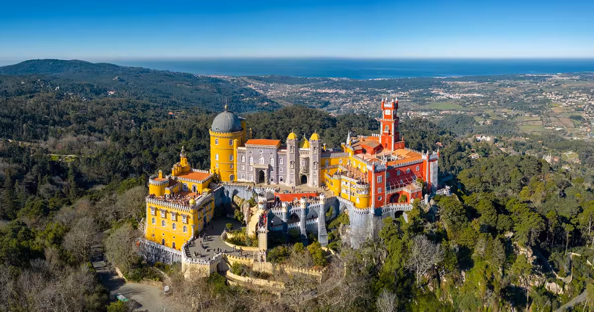 Pena Palace colourful towers rising above Sintra forest with Lisbon skyline beyond