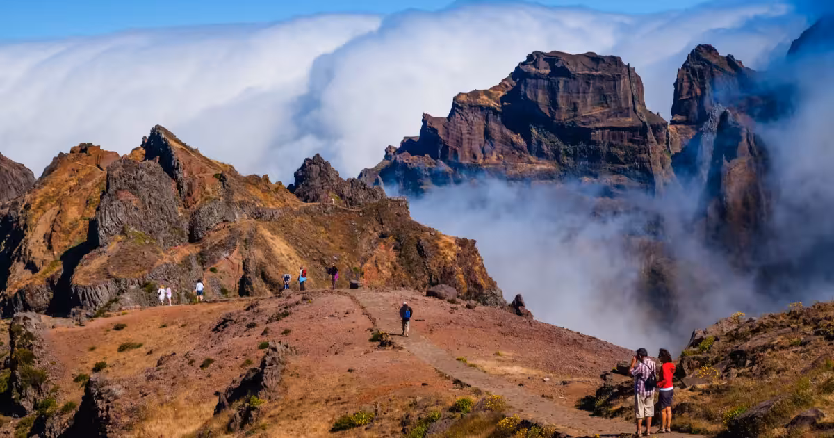 Hikers crossing rocky ridge trail between Pico do Areeiro and Pico Ruivo in Madeira.