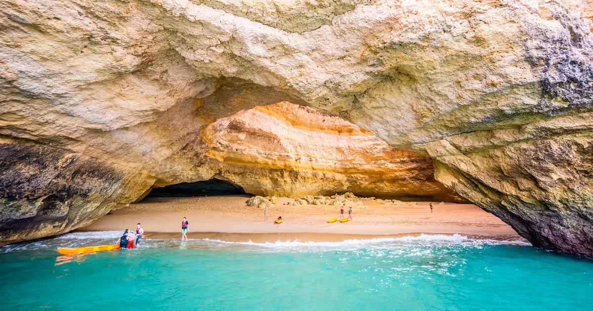 Two kayakers paddling through a sea arch along the Algarve coastline