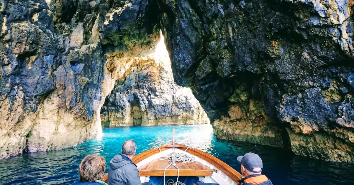Barca privata che si avvicina a una grotta marina calcarea a Sesimbra sulla costa portoghese di Arrábida.