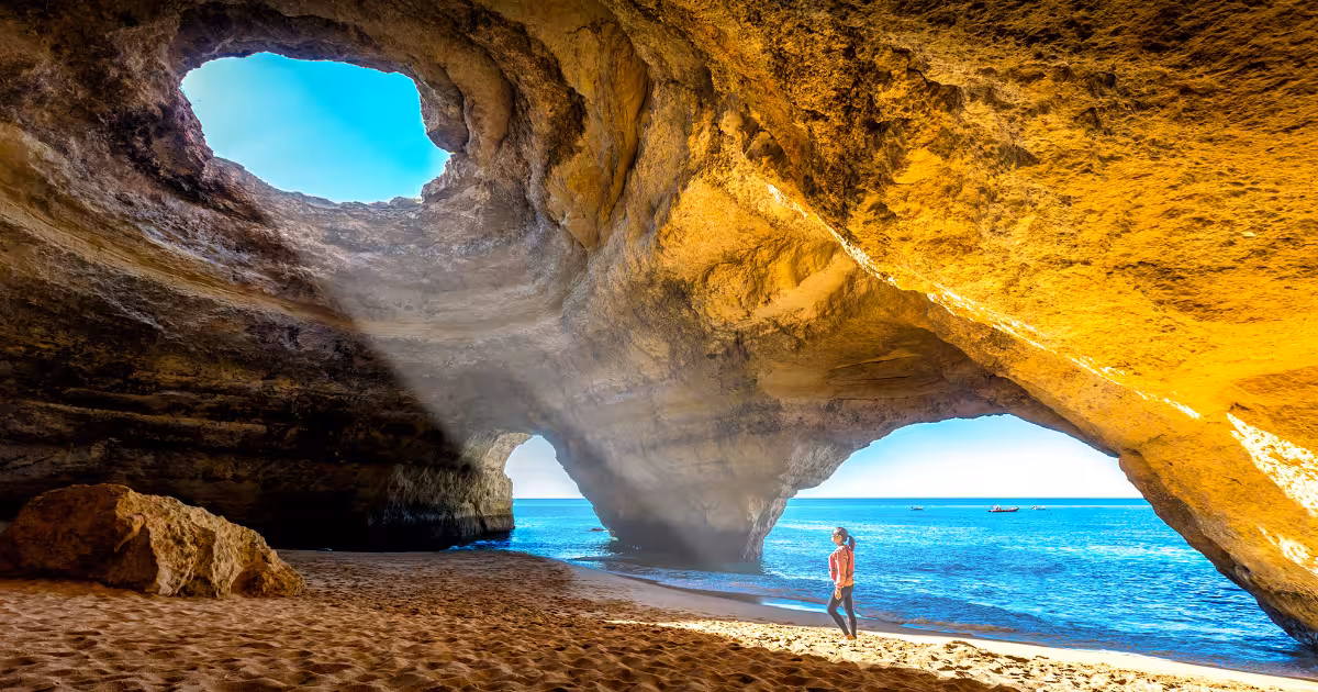 Kayaker entering Benagil Cave at sunrise with golden light through the eye