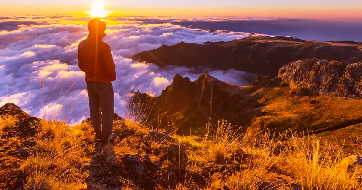 Lone traveller standing on a misty Madeira ridge trail at dawn, facing the Atlantic.