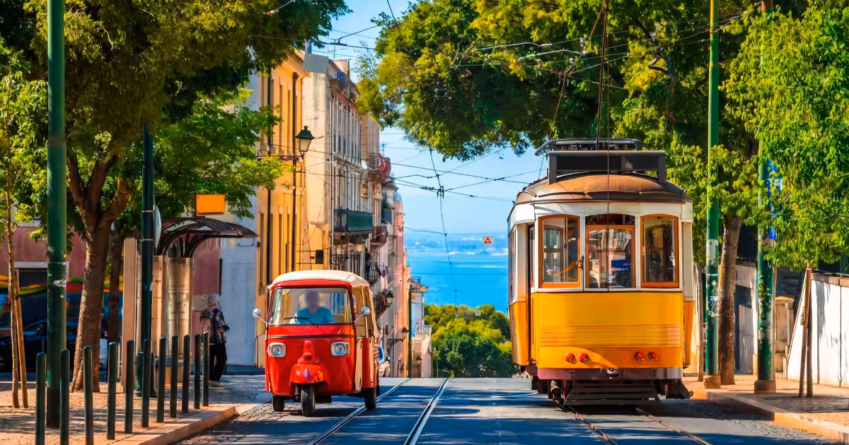 Yellow Tram 28 and a tuk-tuk side by side on a Lisbon cobblestone street.
