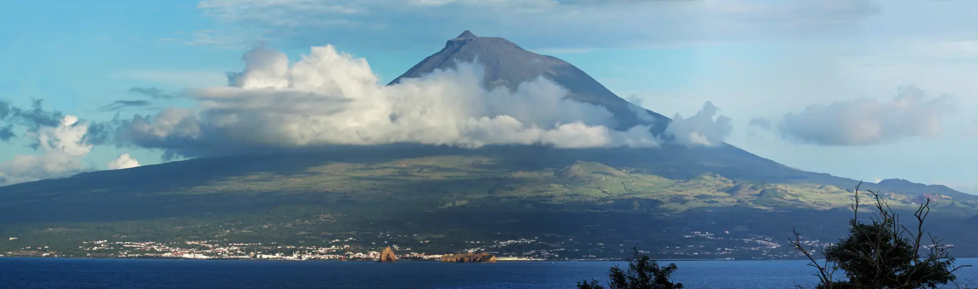 Mount Pico volcanic summit rising above clouds with basalt vineyard walls in foreground.