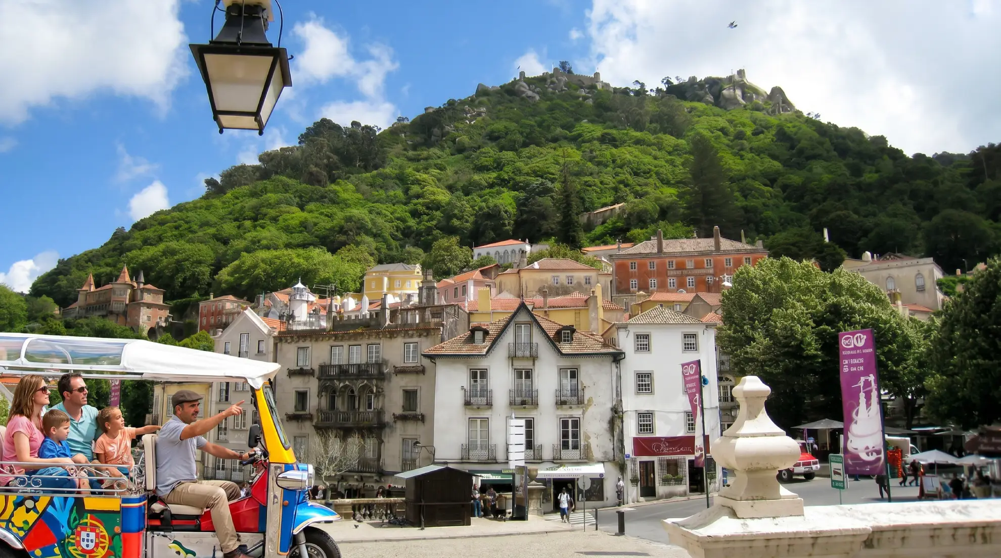 Family in a tuk tuk in Sintra with Pena Palace on hillside above.