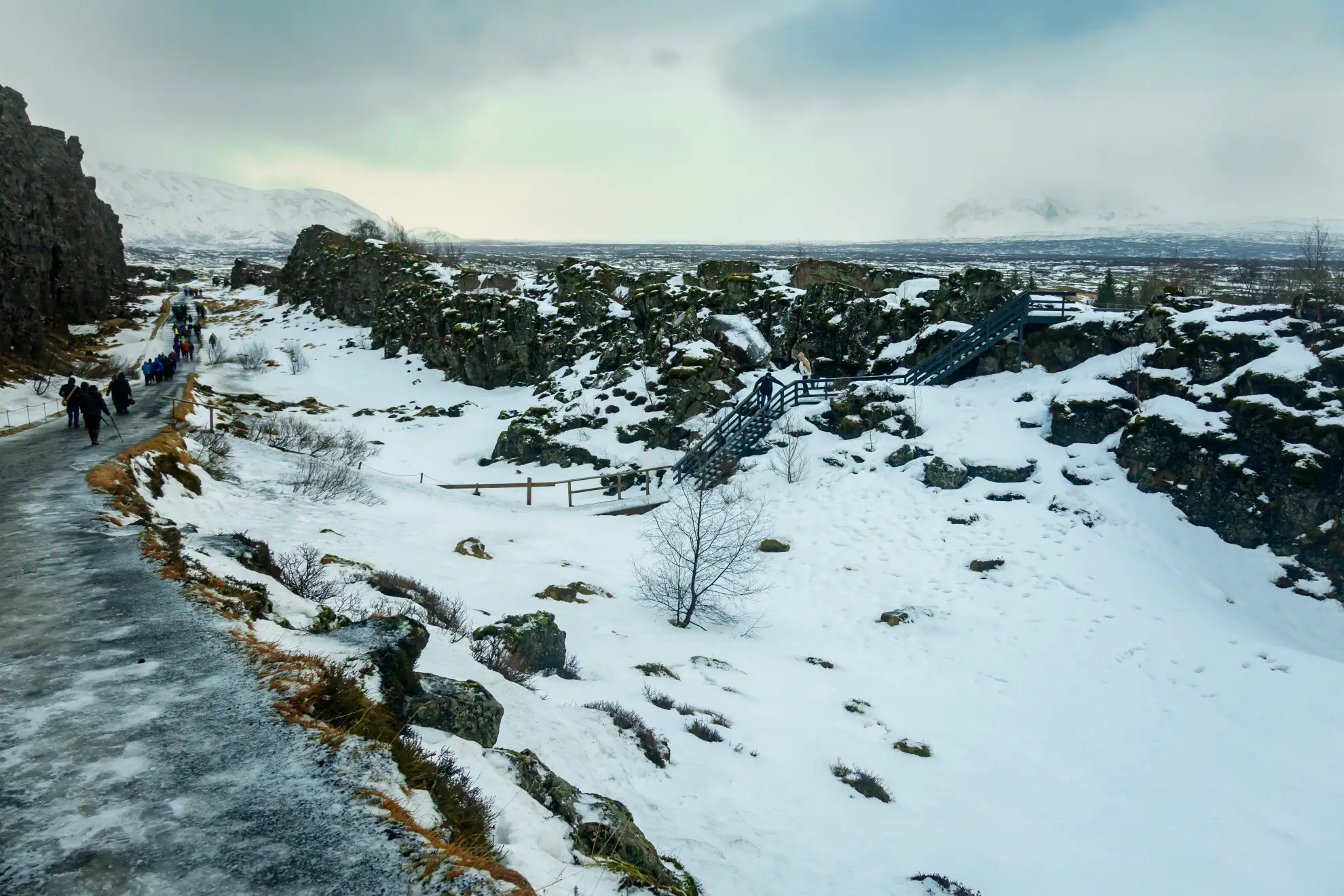 Valle di rift del Parco Nazionale di &THORN;ingvellir innevato con escursionisti visibili in lontananza.