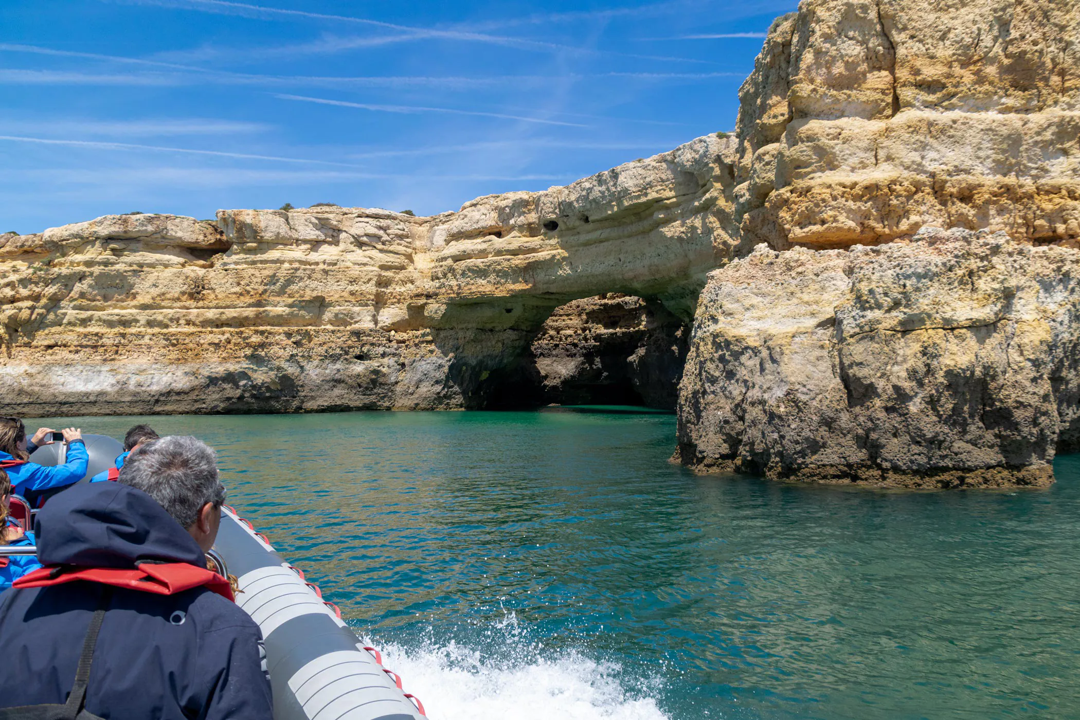 RIB boat navigating a limestone sea arch on the Algarve coast near Albufeira.