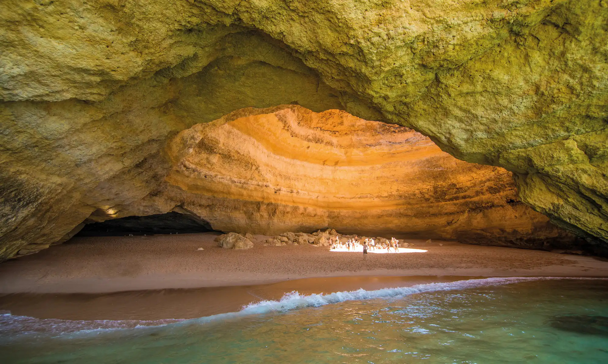 Sunlight falling through the domed ceiling of Benagil Cave onto the interior sand beach.