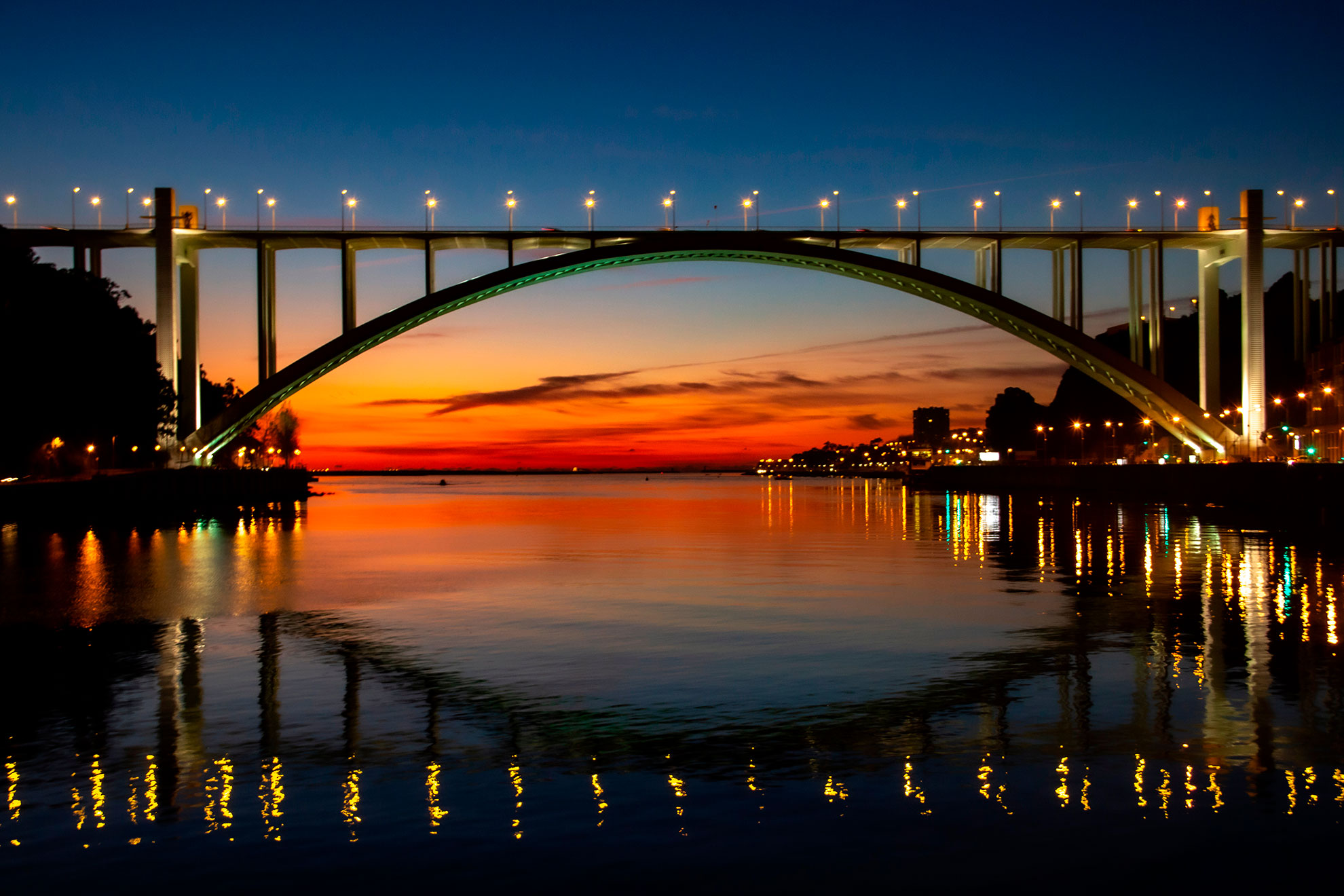 View from sailboat deck toward the Arr&aacute;bida Bridge at sunset on the Douro River.