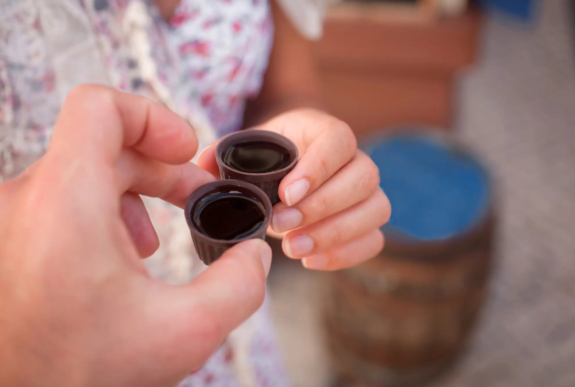 Two hands holding ginjinha cups on cobblestone street in Lisbon