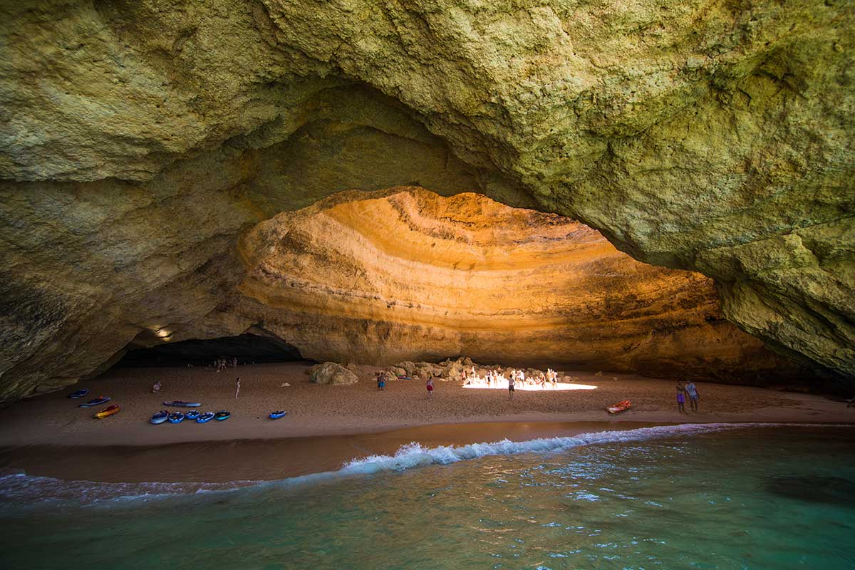 Natural light beam through Benagil cave dome illuminating the interior beach.
