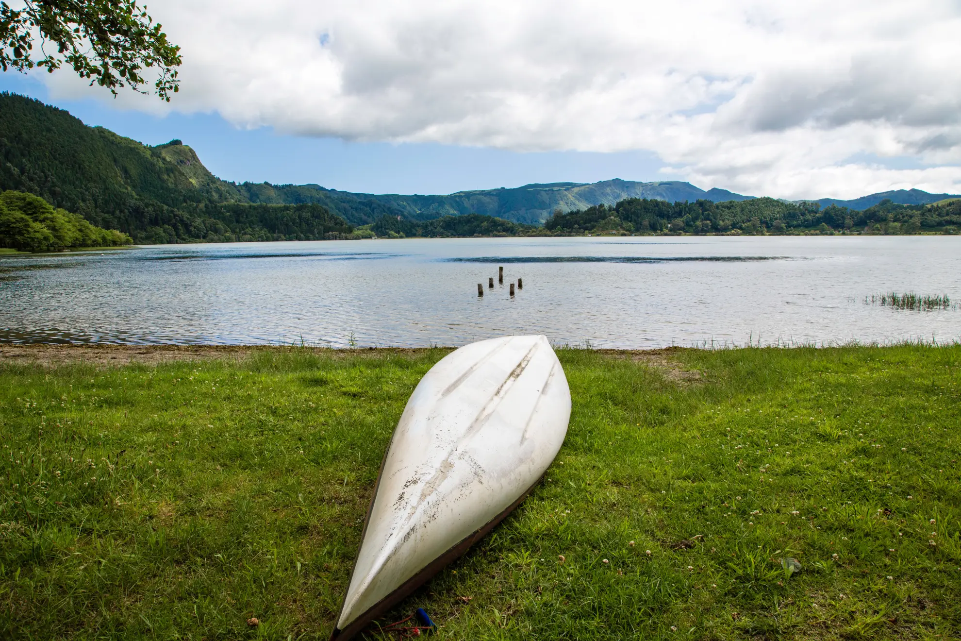 Kayaker on Furnas Lake with geothermal steam rising from fumaroles along the shore.