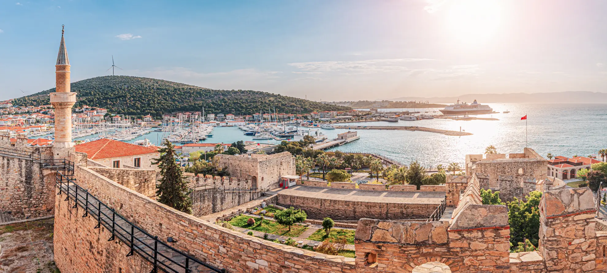 Cesme fortress harbor with Ottoman tower overlooking traditional boats and Greek island vista.