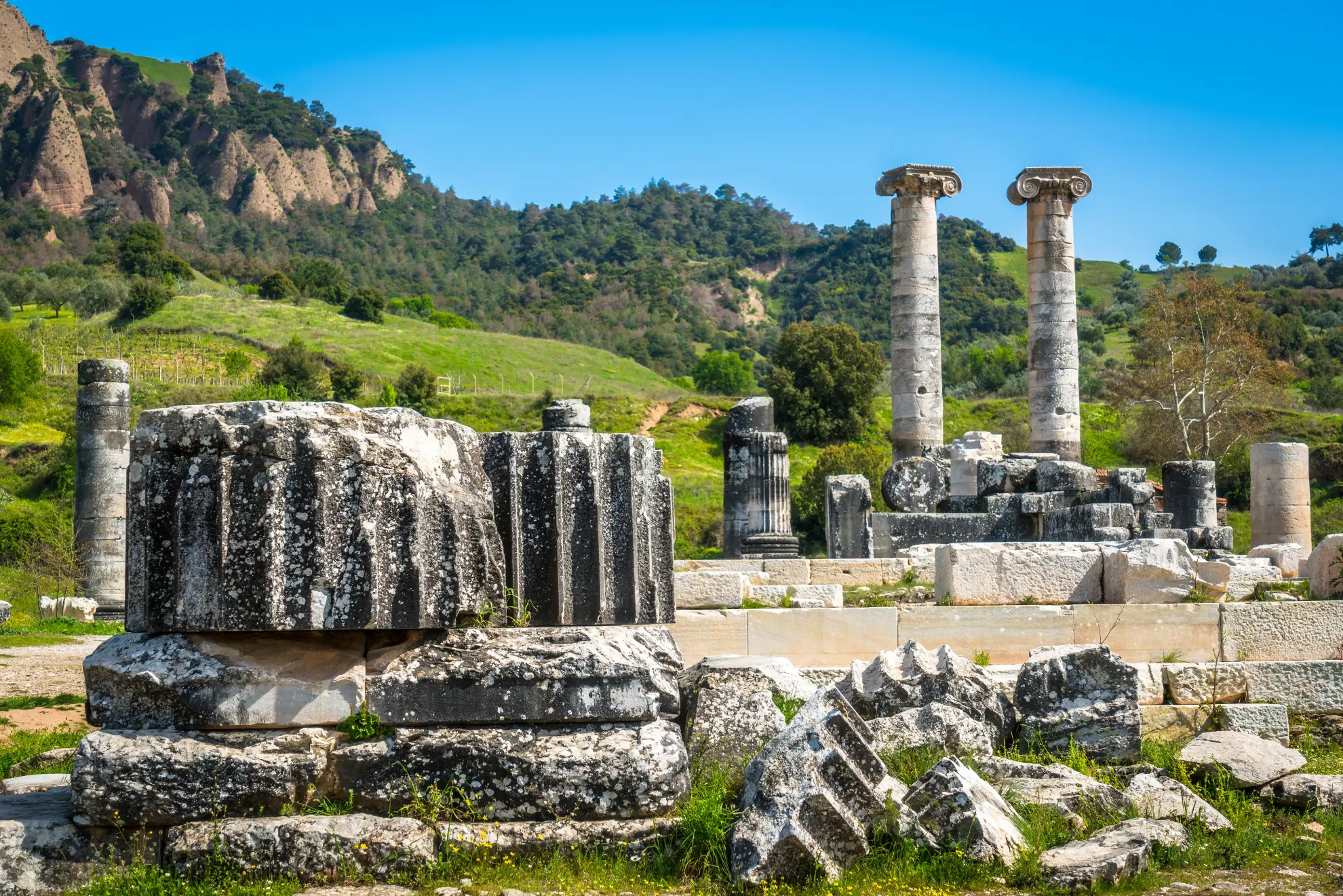 Scattered marble columns and ruins of the Temple of Artemis at Sardis against hilly terrain.