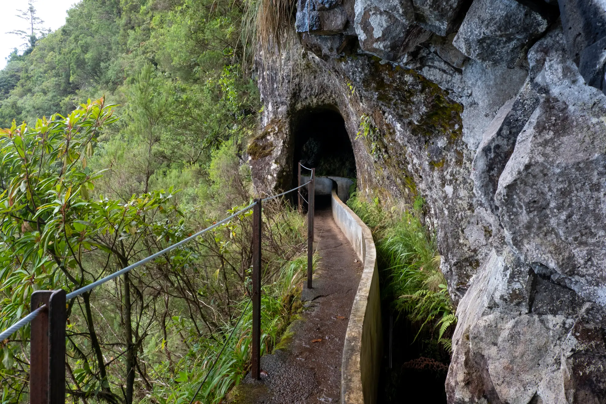 Hiker navigating a narrow exposed ledge on the Levada do Furado trail with valley below.