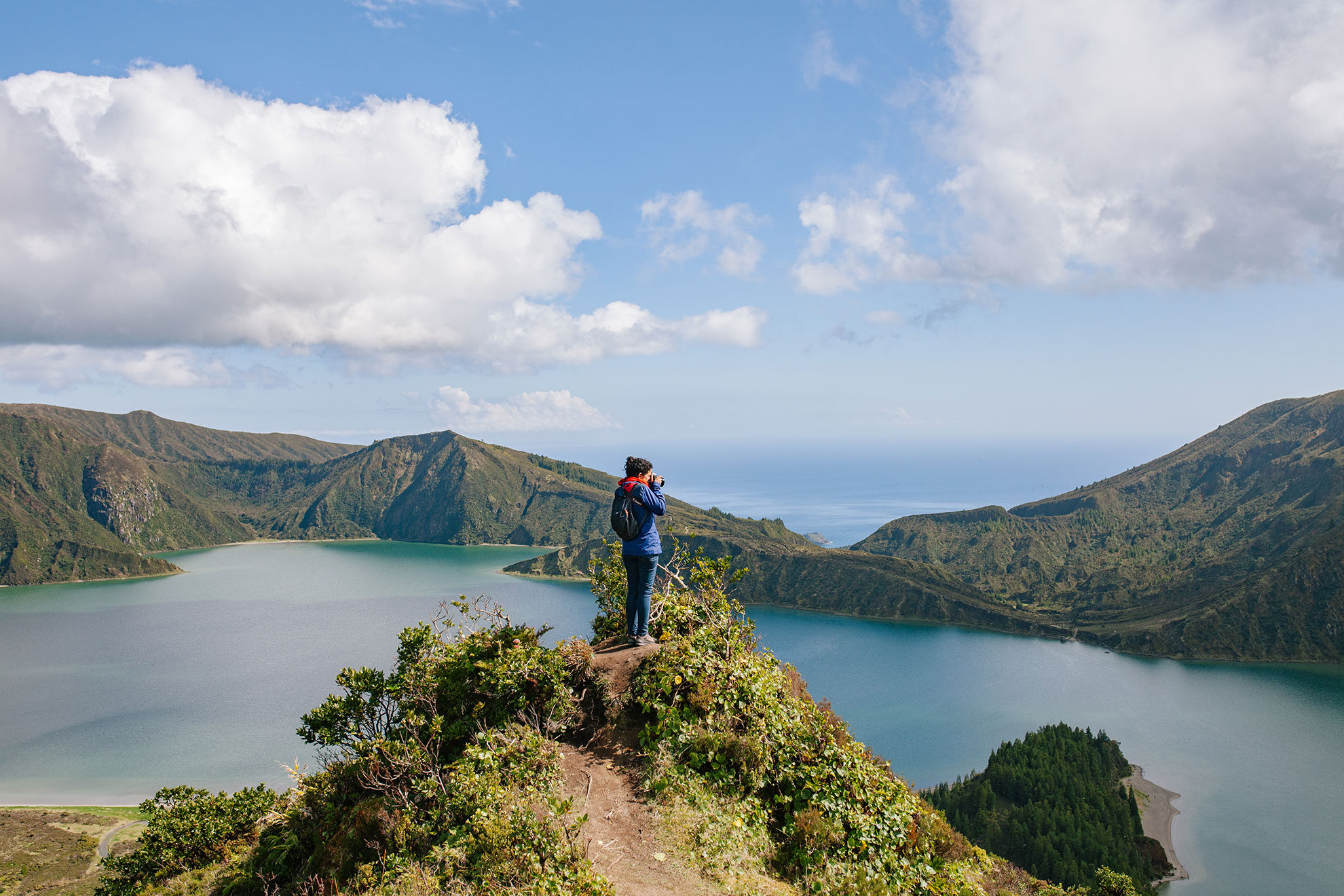 Hiker at the shore of Lagoa do Fogo caldera lake surrounded by green volcanic crater
