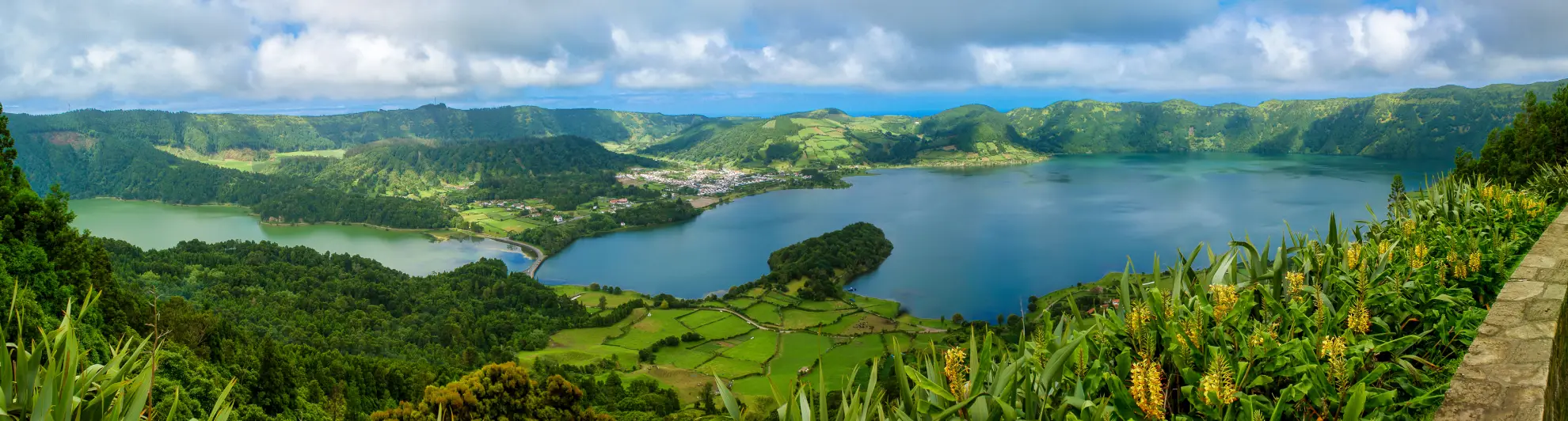 Kayaker on Lagoa Verde with Sete Cidades caldera rim and stone bridge behind.