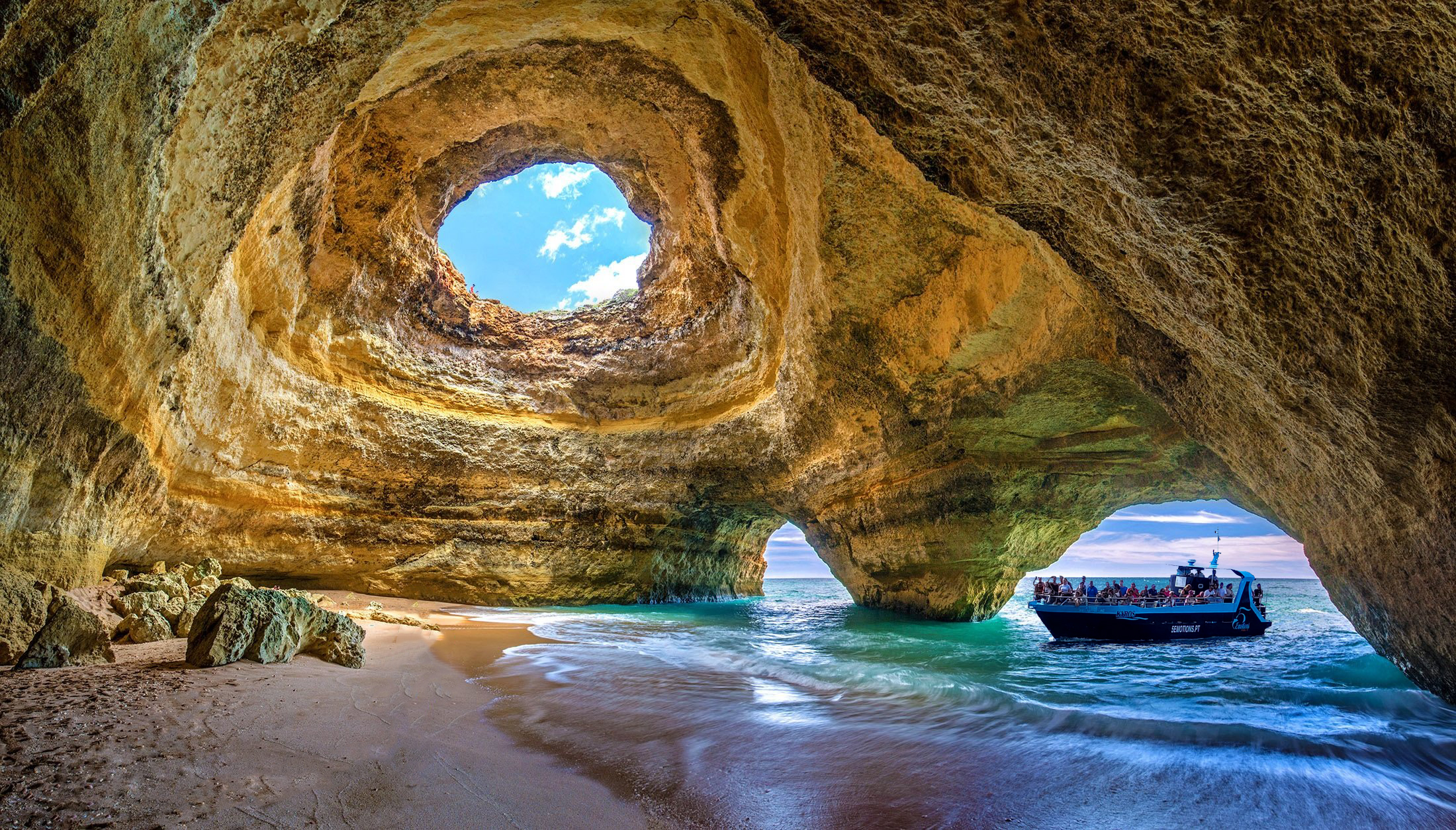Light column through Benagil Cave oculus illuminating the interior sand beach.