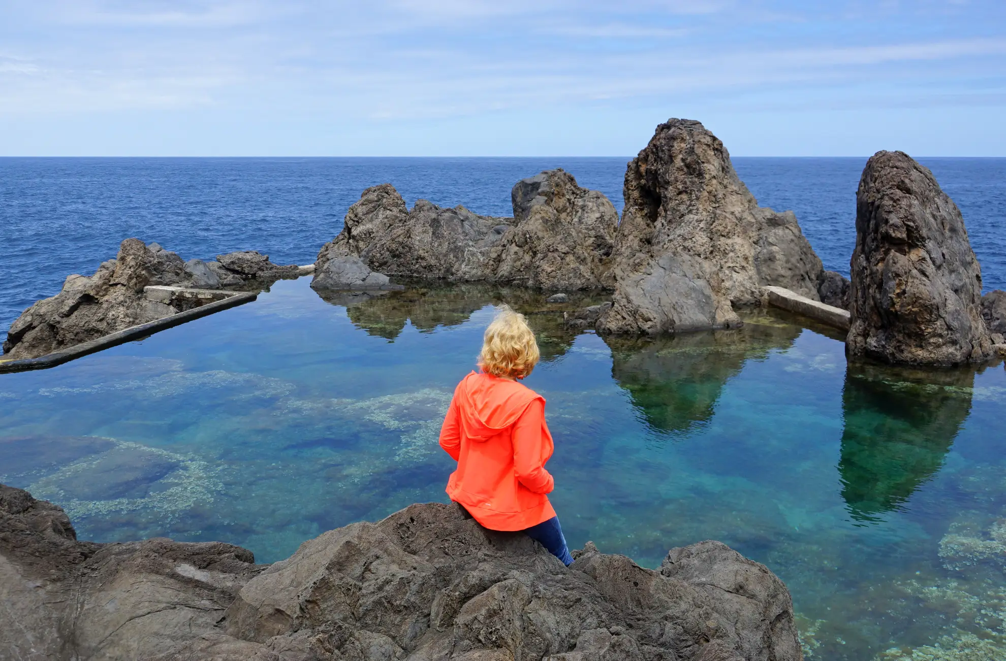Traveler sitting beside Porto Moniz natural volcanic rock pools at dusk Madeira