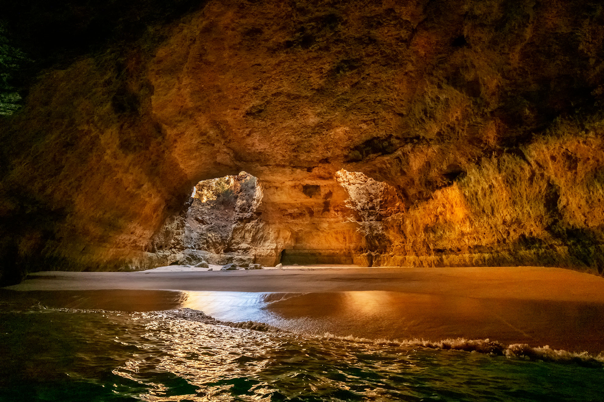 Ochre and rust limestone wall textures inside Benagil Cave lit by sunrise