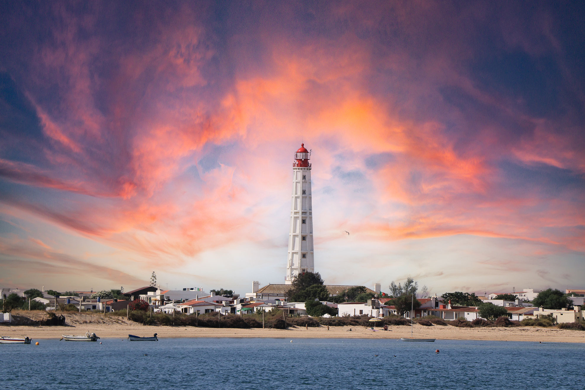 Il faro di Farol sull'Ilha da Culatra che si erge sopra le dune con l'oceano Atlantico sullo sfondo.
