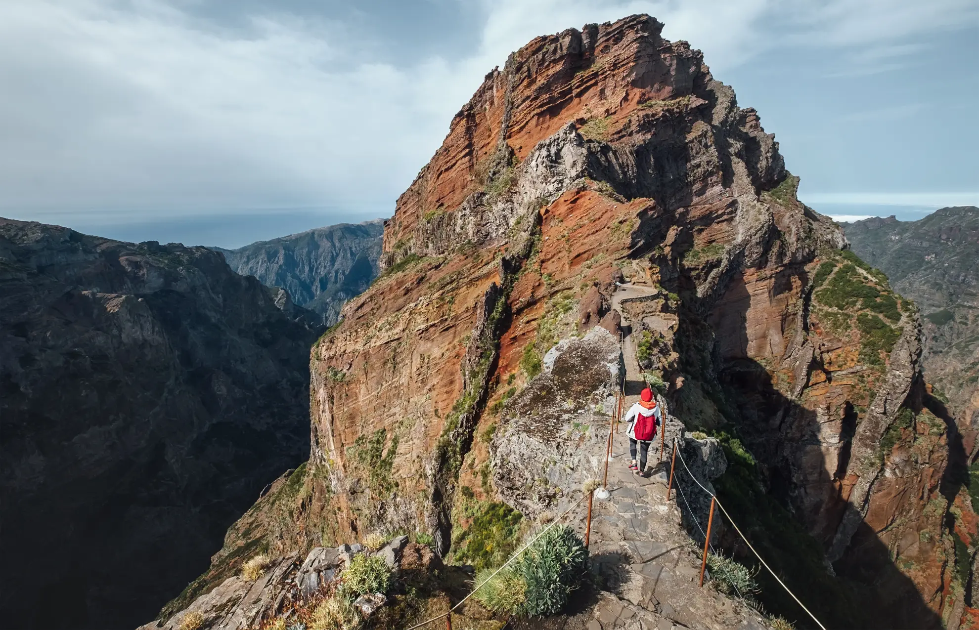 Lone hiker on Madeira ridge trail above cloud layer with Atlantic horizon behind.