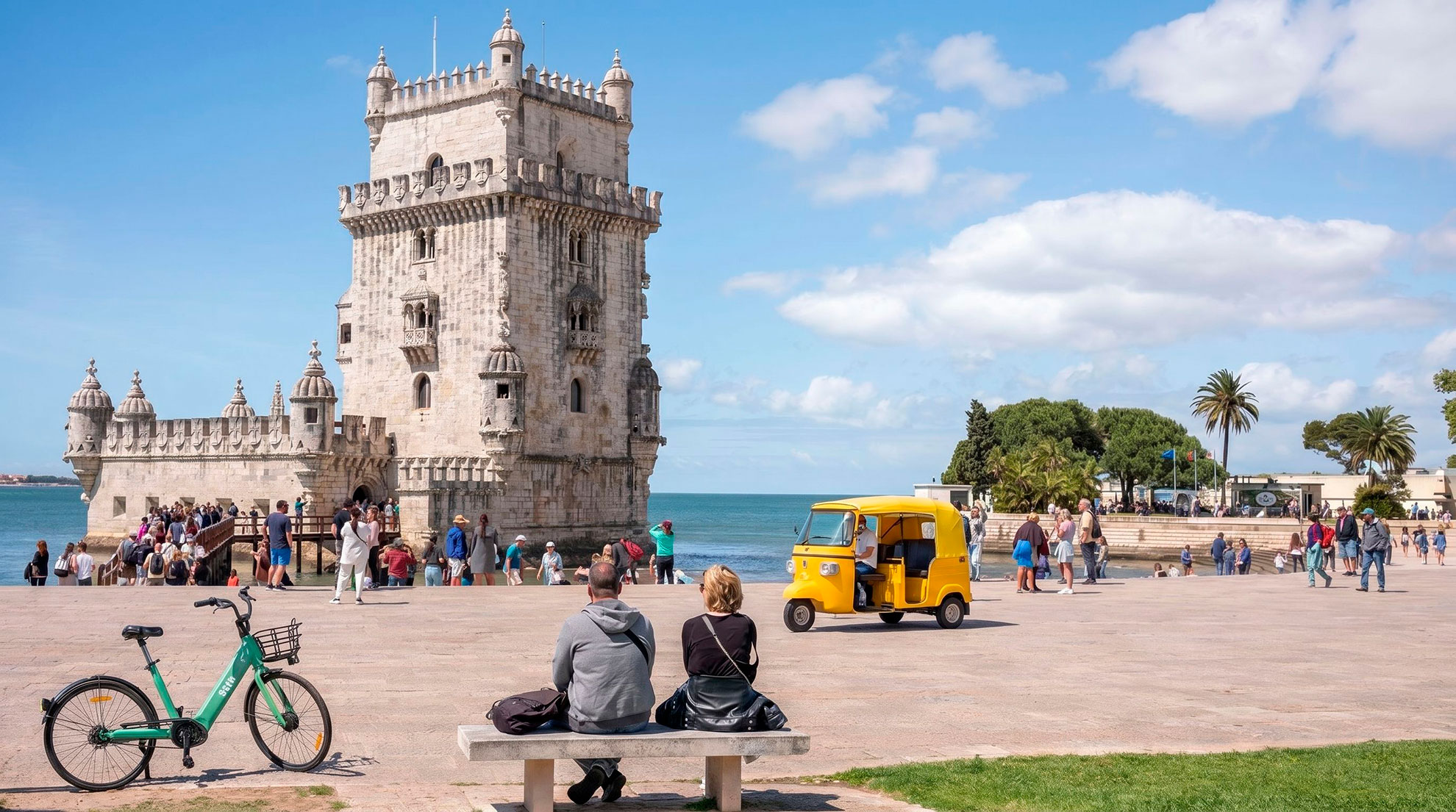 Tuk tuk driver pointing toward Torre de Bel&eacute;m with passengers on Lisbon riverfront