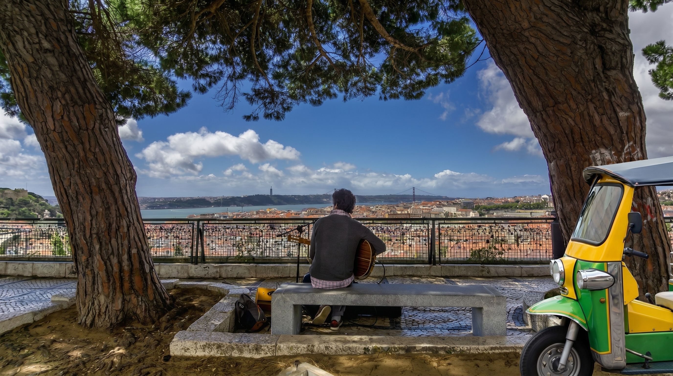Tuk-tuk parked at Senhora do Monte viewpoint overlooking Lisbon's historic rooftops.