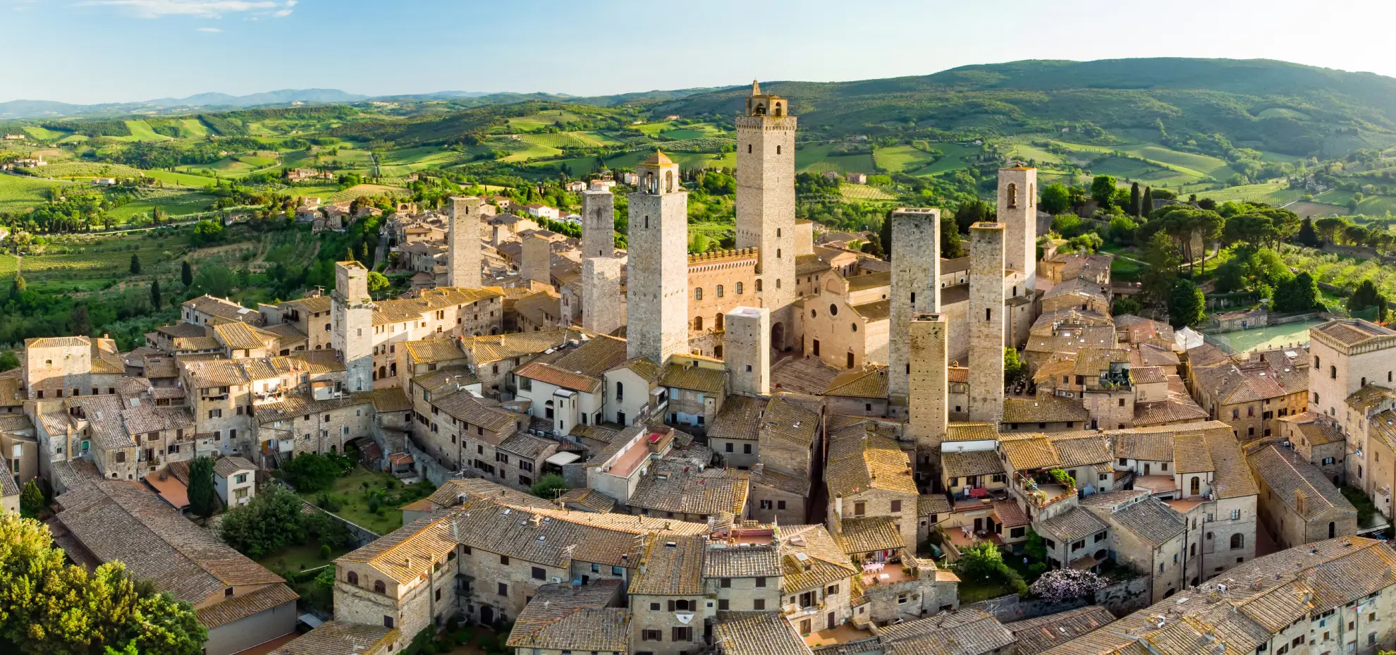 Medieval towers of San Gimignano rising above Tuscan vineyards at golden hour.