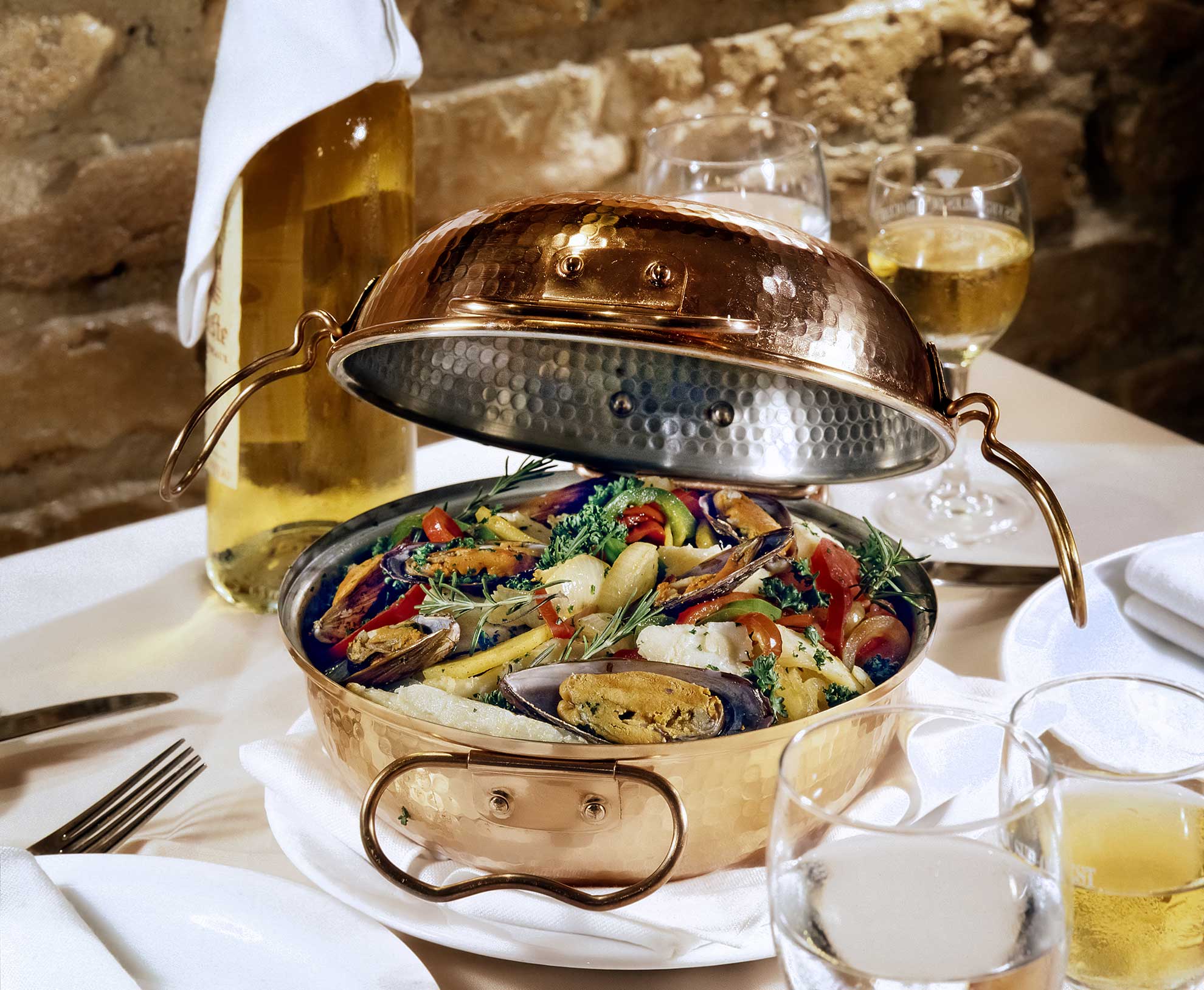 Open copper cataplana with clams and fish beside a bottle of Algarve ros&eacute;.