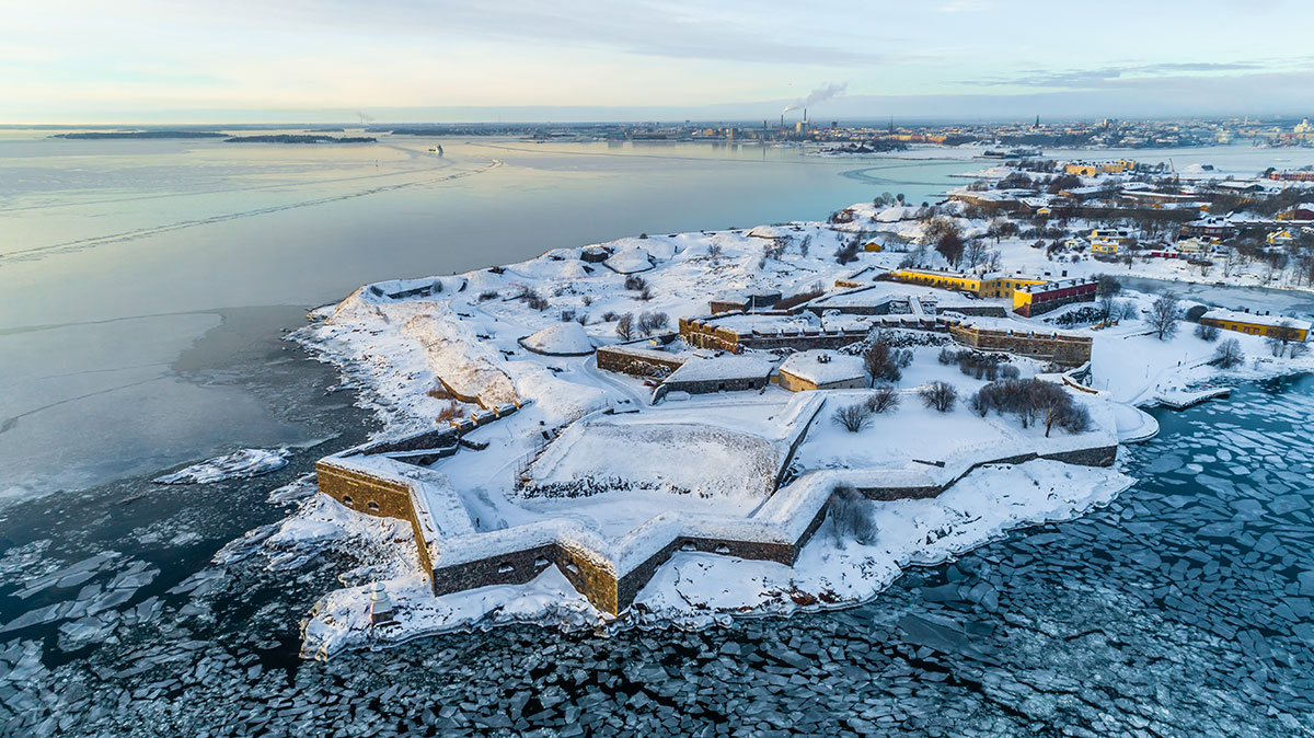 Suomenlinna covered in snow, with fortification walls and pathways leading into the winter landscape.
